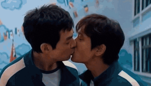 two men are kissing each other on the cheek in a hallway .