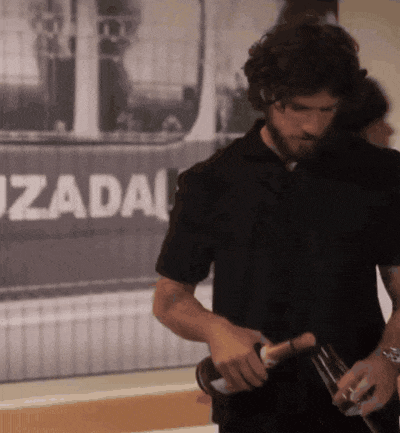 a man in a black shirt is holding a bottle of wine in front of a sign that says uzadai
