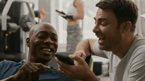 two men are laughing while looking at a cellphone