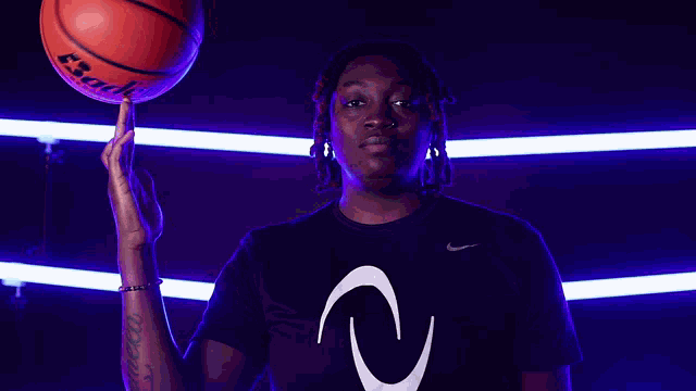 a man in a black nike shirt is holding a basketball on his finger