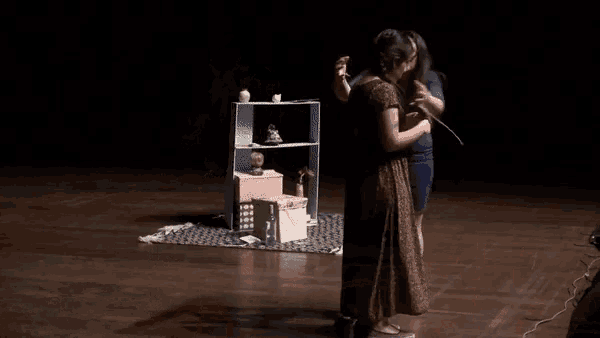 two women hugging on a stage in front of a bookcase