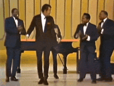 a group of men in suits and bow ties are dancing on a stage in front of a piano .