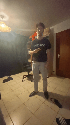 a man wearing a kenzo shirt is standing in a dark room