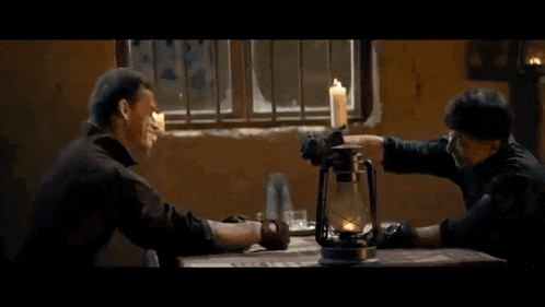 two men are sitting at a table with a candle and a lantern .