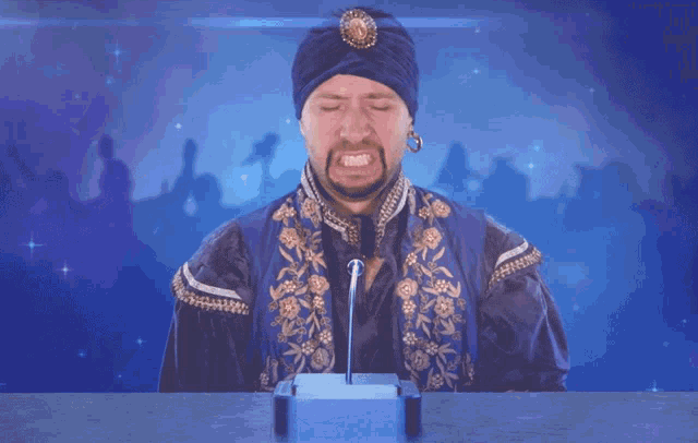 a man in a turban is sitting at a table with a microphone