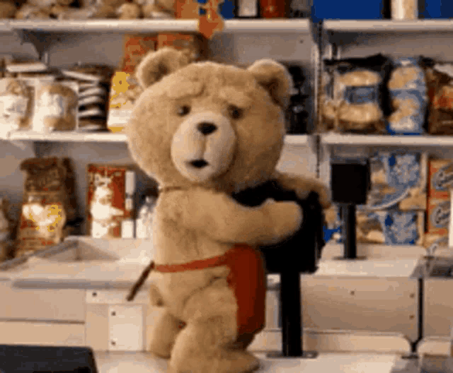 a teddy bear wearing a red apron is standing in a store .