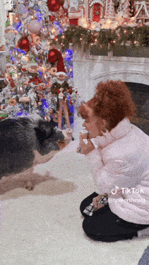 a woman kneeling down with a pig in front of a christmas tree and fireplace