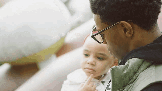 a man wearing glasses is holding a little girl in his arms