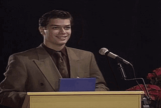 a man in a suit and tie stands behind a podium with a microphone