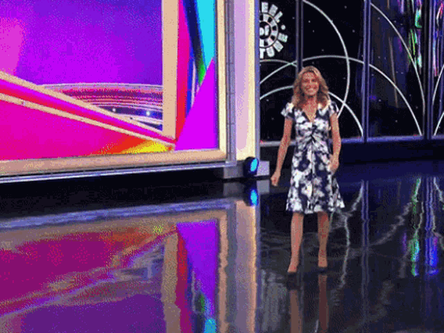 a woman in a blue and white dress is standing in front of a large screen
