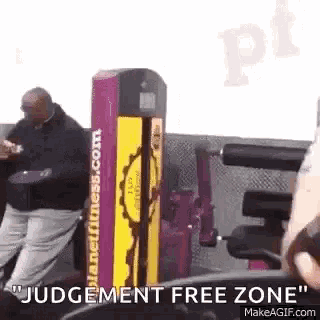a man is sitting at a table in a gym with a judgement free zone machine in the background .