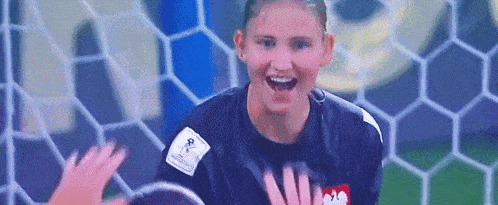 a female soccer goalie is smiling while standing in front of a soccer net .