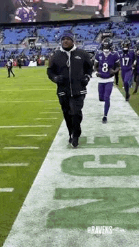 a man is running on a football field with players in purple jerseys .
