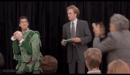 two men in suits are standing on a stage in front of a crowd .