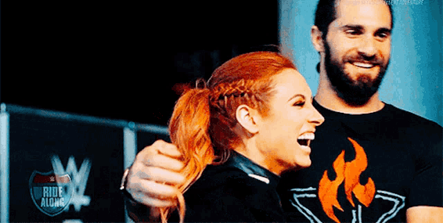a man and a woman are laughing together and the man is wearing a shirt that says ride alone .