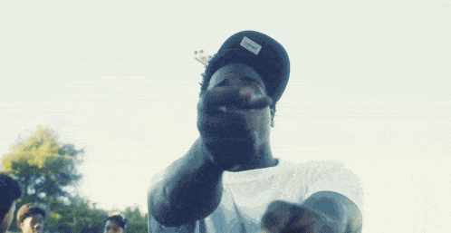 a man wearing a white shirt and a black hat with the word nike on it points at the camera