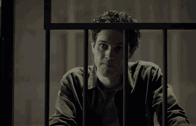 a man in a prison cell behind bars looks at the camera