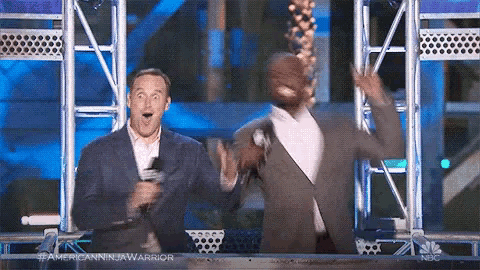 two men in suits are standing next to each other on a stage with their hands in the air .