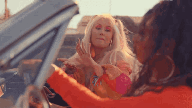 two women are sitting in a car and one of them is wearing a pink top