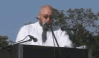 a man in a white shirt and tie is speaking into a microphone .