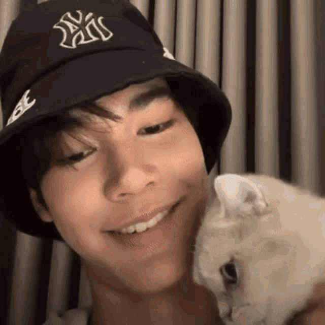 a young man wearing a ny hat is holding a cat .