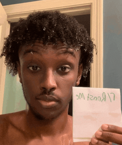 a man with curly hair is holding up a piece of paper that says ' sm f00a17 ' on it