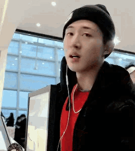 a young man wearing a beanie and earphones looks at the camera