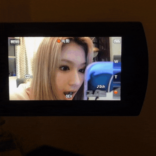 a woman 's face is being recorded on a camera with a menu button in the corner