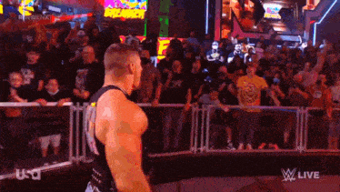 a man in a black tank top stands in front of a crowd at a wrestling event