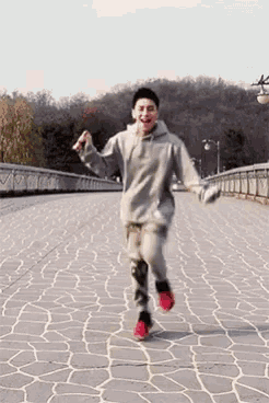 a young man in a grey hoodie is running across a bridge