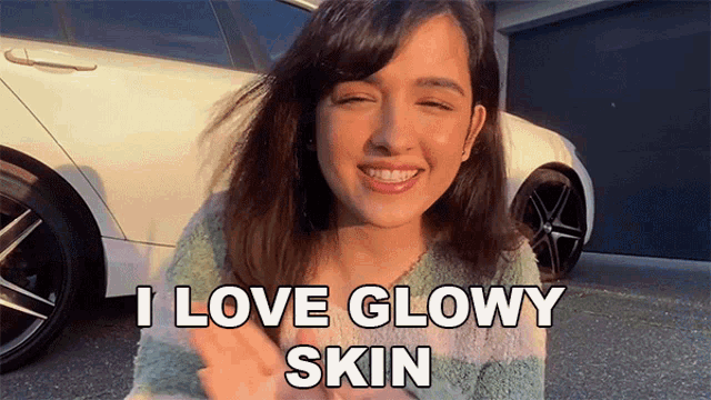 a woman says i love glowy skin while standing in front of a white car