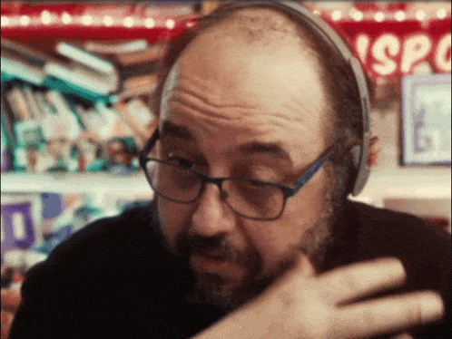 a bald man wearing glasses and headphones with a sign in the background that says sp