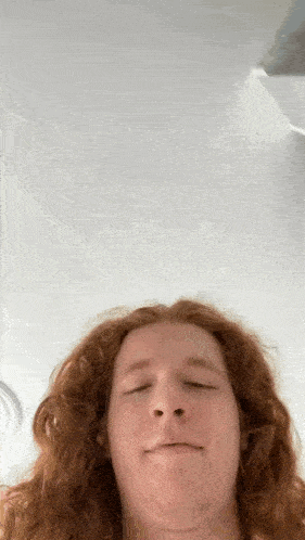 a young man with long red hair is making a funny face .