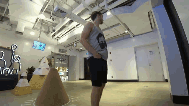 a man in a tank top with a batman logo stands in a room