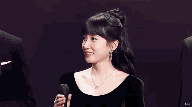 a woman in a black dress is holding a microphone in front of her face