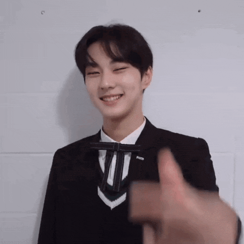 a young man in a suit and tie is smiling and giving a thumbs up sign .
