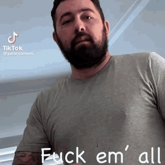 a man with a beard is wearing a grey shirt and says " fuck em " all