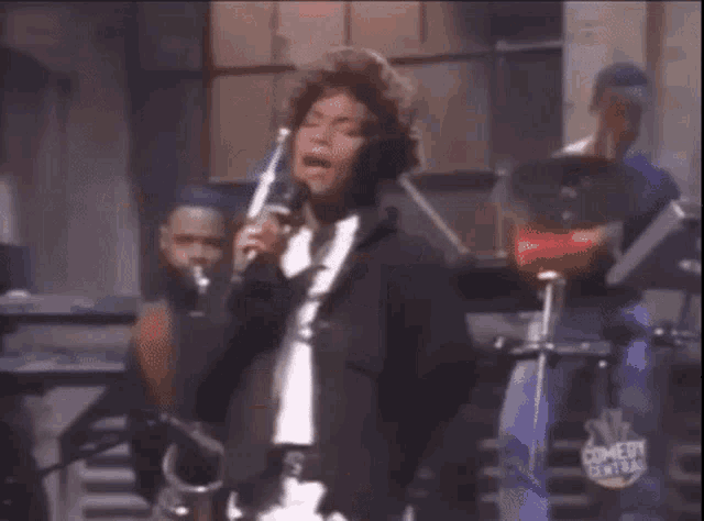 a woman is singing into a microphone while a band plays behind her .