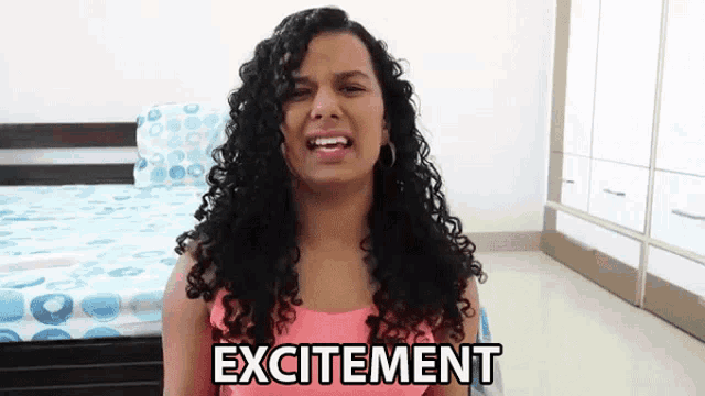 a woman with curly hair is saying excitement in front of a bed .