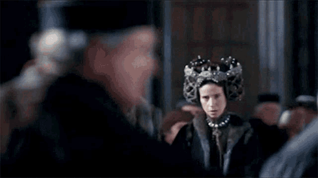 a woman with a crown on her head is standing in front of a crowd of people .