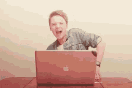a man is laughing while sitting in front of a laptop computer .