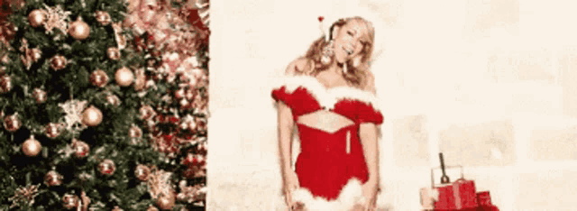 a woman in a santa costume is standing next to a christmas tree