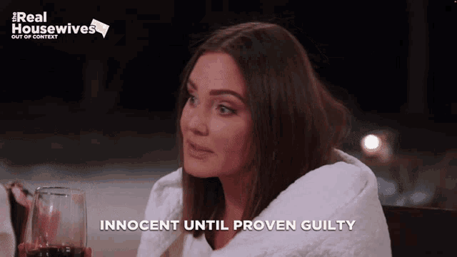 a woman is wrapped in a white blanket and holding a glass of wine with the words innocent until proven guilty below her