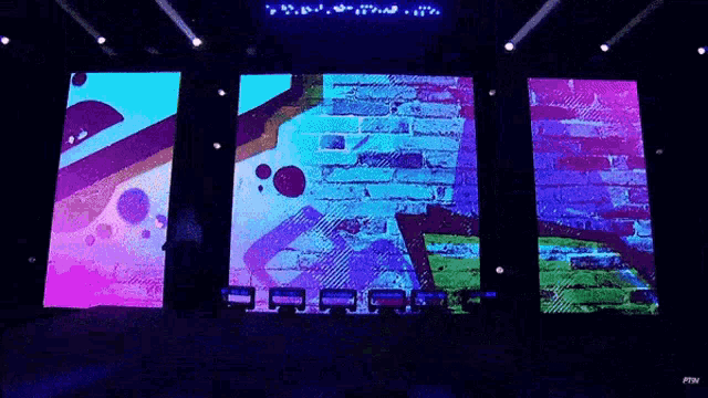 a man is standing on a stage in front of three large screens with graffiti on them .