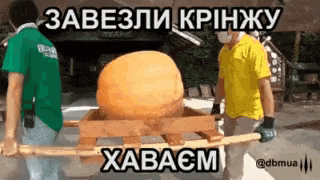 two men are carrying a large orange ball on a wooden platform .