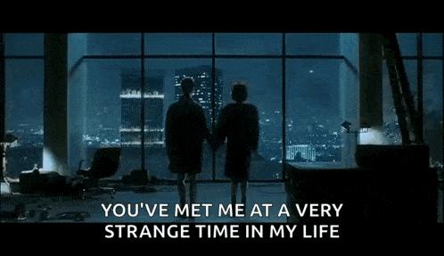 a man and a woman are standing in front of a large window holding hands and looking out at the city .
