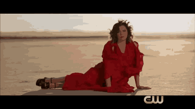 a woman in a red dress is laying on the ground with the cw logo behind her