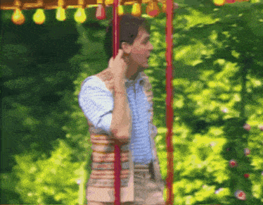 a man in a striped vest is talking on a cell phone while standing on a swing