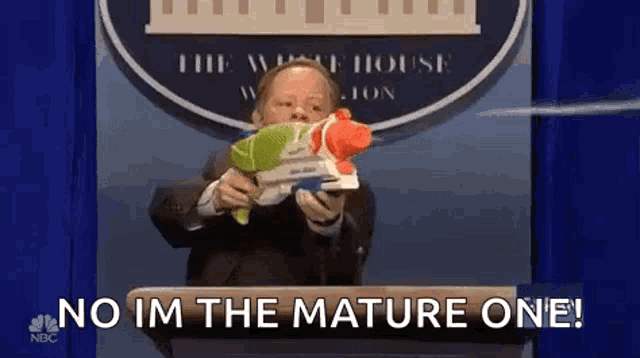 a man in a suit is holding a water gun and saying `` no im the mature one ! ''