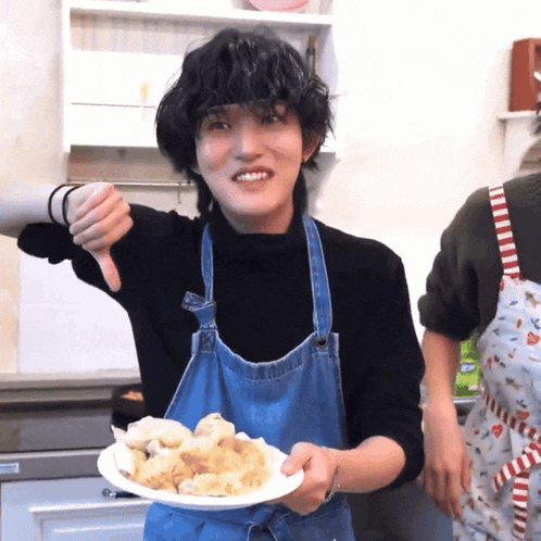 a person wearing an apron is holding a plate of food and giving a thumbs down sign